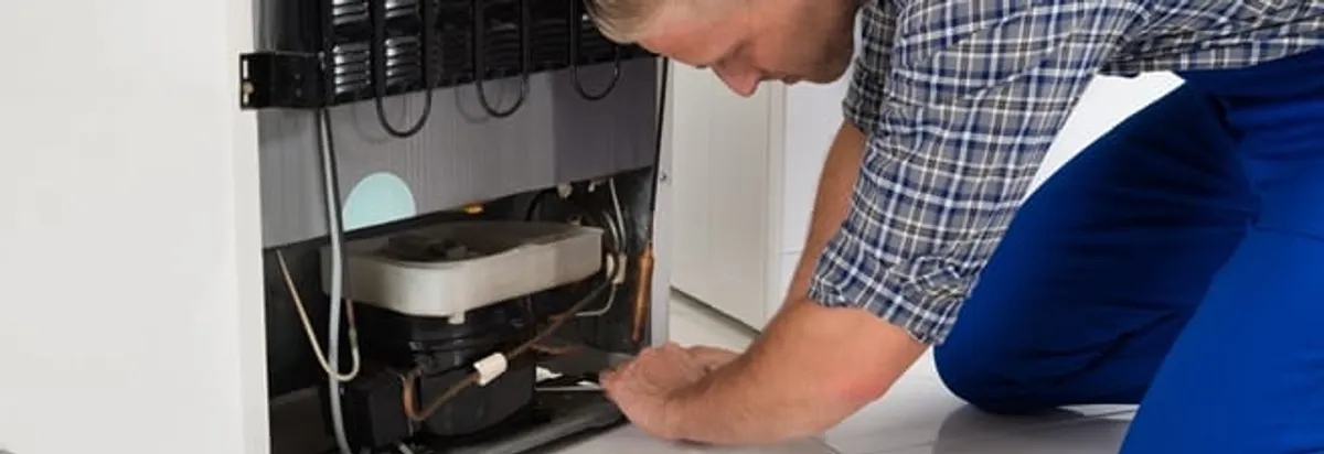 Refrigerator repair technician servicing the compressor and condenser area in Phoenix, AZ